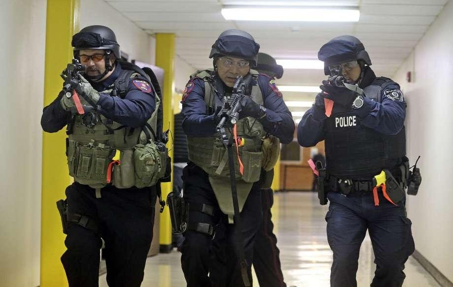 Police officers in swat gear walk down a hallway holding rifles